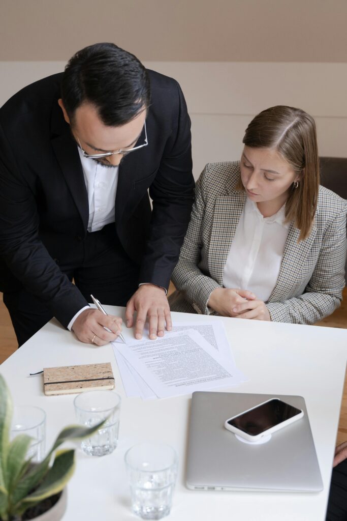 Two business professionals signing a contract at a desk; collaborating in an office.